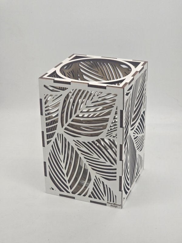 Ljuslyktan Saga i vit – handgjord trälykta med lövmotiv som sprider ett mjukt och harmoniskt ljus. Tillverkad i Sverige av Nordland Design.