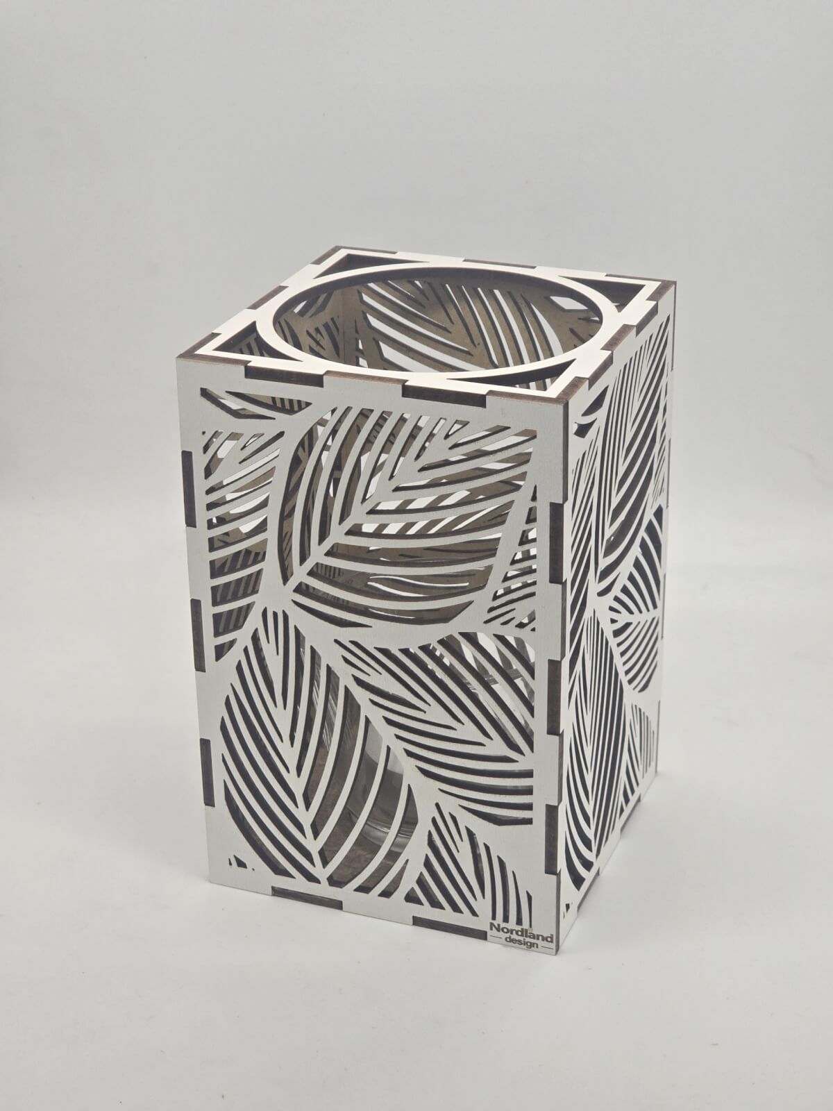 Ljuslyktan Saga i vit – handgjord trälykta med lövmotiv som sprider ett mjukt och harmoniskt ljus. Tillverkad i Sverige av Nordland Design.