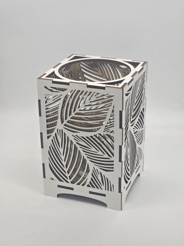 Ljuslyktan Saga i vit – handgjord trälykta med lövmotiv som sprider ett mjukt och harmoniskt ljus. Tillverkad i Sverige av Nordland Design.