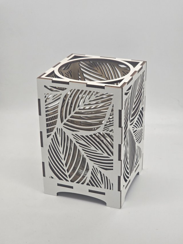 Ljuslyktan Saga i vit – handgjord trälykta med lövmotiv som sprider ett mjukt och harmoniskt ljus. Tillverkad i Sverige av Nordland Design.